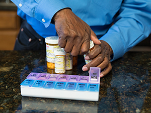 Closeup of hands filling pill organizer with medicines.
