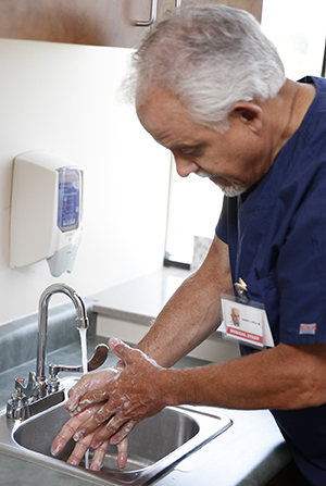 Healthcare provider washing hands in sink.