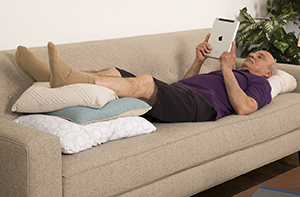 Man lying on couch with legs elevated on pillows.