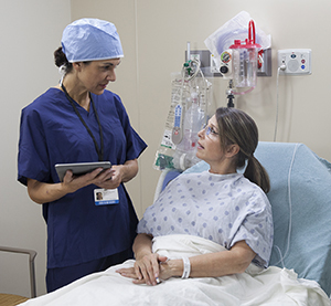 Healthcare provider talking to woman in pre-op hospital room.