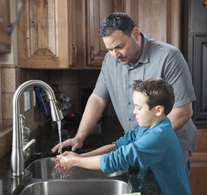 Man helping boy wash his hands in kitchen sink.