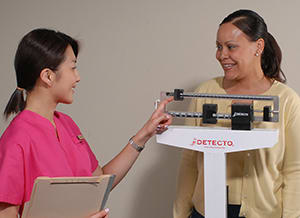 Healthcare provider weighing woman on scale.