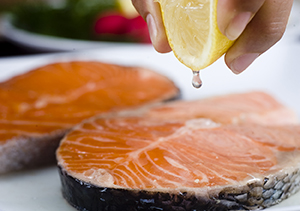 Closeup of hand squeezing lemon juice onto salmon steak.