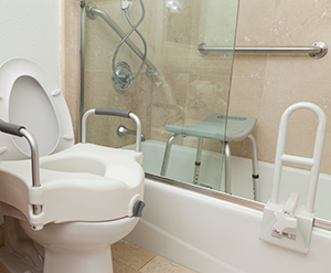 Toilet with modified seat, shower chair, grab bar and handheld water nozzle in bathroom.