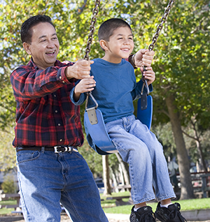 Man pushing boy on swing in park.