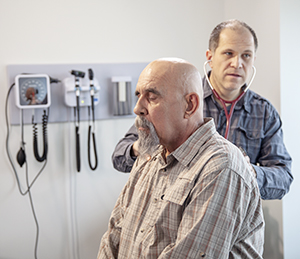 Doctor pressing stethoscope to man's back and listening.