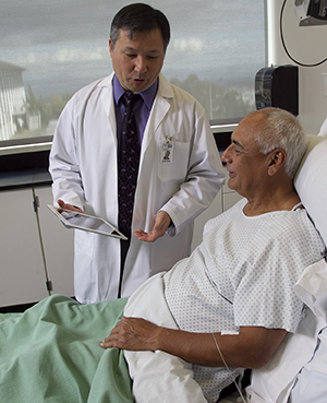 Healthcare provider with electronic tablet talking to man in hospital bed.