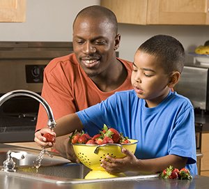 Man and boy washing strawberries in sink.