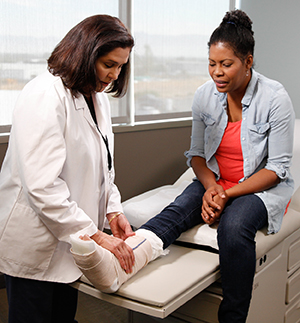 Healthcare provider examining cast on woman's leg.