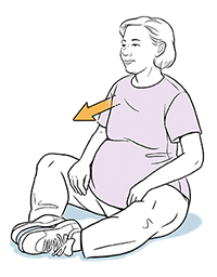 Pregnant woman sitting on floor doing tailor sit exercise.