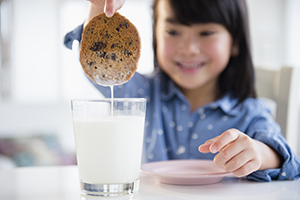 Young girl dunking a cookie in a glass of milk.