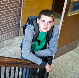 Teenaged boy in the stairwell of a high school looking up to the camera.