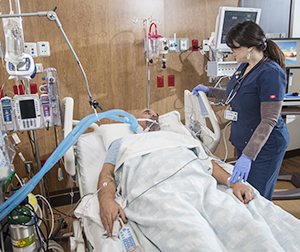 Healthcare provider caring for intubated man in intensive care unit bed.