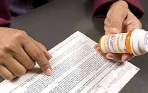 Closeup of hands with prescription information and prescription pill bottle.