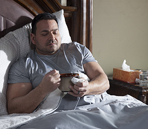 Man sitting in bed with a cup of soup.