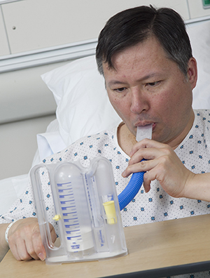Man using incentive spirometer in hospital bed.