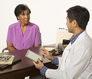 Healthcare provider with electronic tablet talking to woman.
