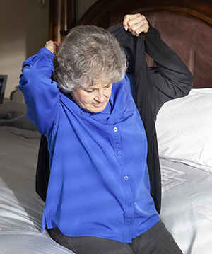Woman sitting on bed, putting on jacket.