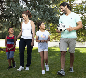 Man, woman, girl and boy walking in park with soccer ball.