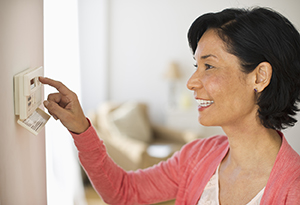 Woman adjusting temperature of air conditioning thermostat.
