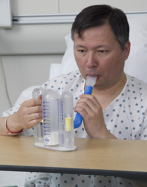 Patient in hospital bed using incentive spirometer.