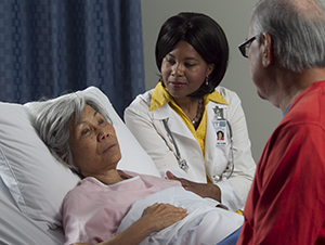 Woman lying in hospital bed, man and healthcare provider sitting next to bed.