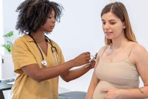 En el consultorio de un médico, el médico administra una vacuna en la parte superior del brazo de una mujer embarazada.