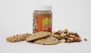 Una barrita de muesli, un tarro de mantequilla de cacahuate, galletas y frutos secos variados.