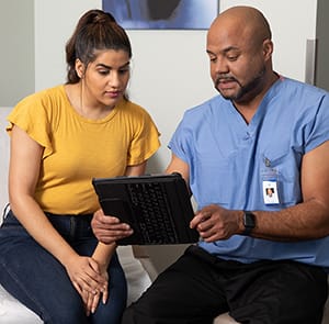 Doctor and woman looking at electronic tablet in exam room.
