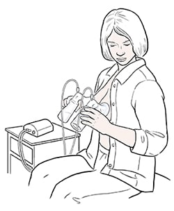 Female sitting in chair expressing milk from both breasts with electric double breast pump.
