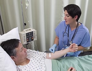 Man lying in hospital bed with I.V. in arm. Health care provider is checking IV.