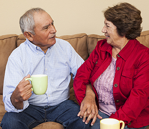 Two older people sitting on couch, holding hands, and talking.